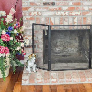A cozy brick fireplace with a floral arrangement and a ceramic cat figurine.