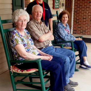 A group of seniors sitting on rocking chairs on a porch.