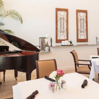A cozy restaurant dining area featuring a grand piano and elegantly set tables with floral centerpieces.