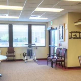 A waiting room with several chairs, a bicycle exercise machine, and large windows letting in natural light.