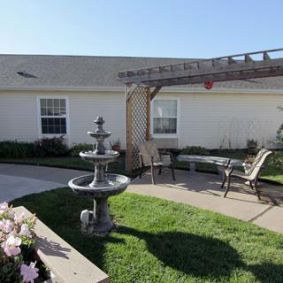 A tranquil garden patio with a central fountain, pergola, and seating area.