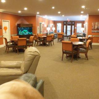 A cozy lounge area with multiple tables and chairs, a television, and warm lighting.