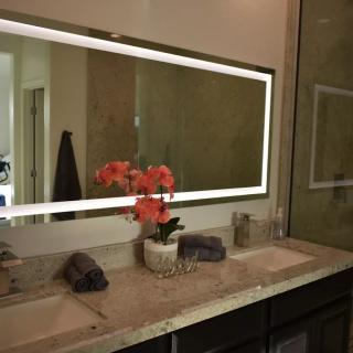 A modern bathroom with a large illuminated mirror, a marble countertop, and decorative flowers.