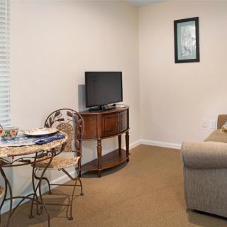 A cozy living room with a TV on a wooden stand, a sofa, and a small dining table with chairs.
