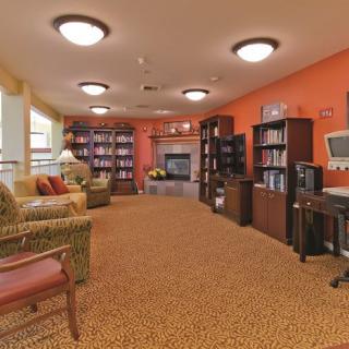 A cozy living room with bookshelves, comfortable seating, and a desk with a computer, illuminated by warm lighting.
