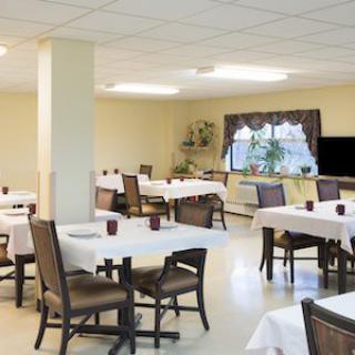 A well-lit dining area with neatly arranged tables and chairs, featuring white tablecloths.