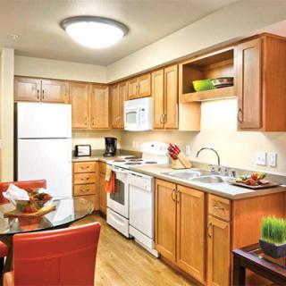 A modern kitchen with wooden cabinets, complete with appliances and a small dining area.