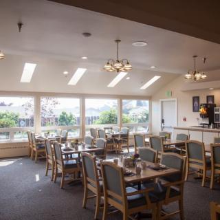 A bright dining area with tables and chairs arranged near large windows, allowing natural light to fill the space.