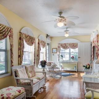 A bright sunroom featuring wicker furniture, hardwood flooring, and large windows with patterned curtains.