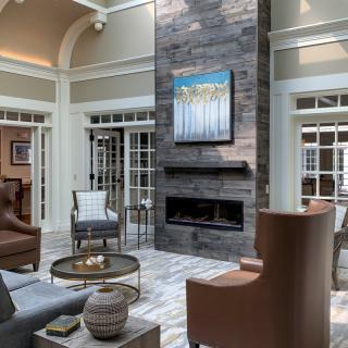 A modern living room featuring a tall stone fireplace, elegant seating, and large windows.