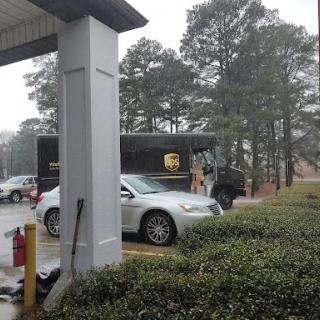 A UPS delivery truck parked in a rainy area with a silver car nearby.