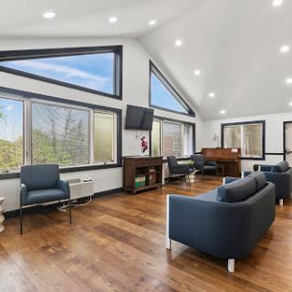 A modern lounge area featuring large windows for ample natural light, stylish furniture, and a warm wooden floor.