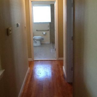 A view of a hallway with a wooden floor leading to a bathroom.