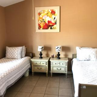 A cozy bedroom featuring two twin beds with matching nightstands and decorative lamps, complemented by a floral painting on the wall.