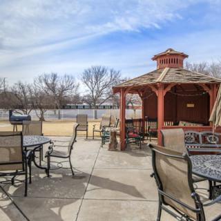 An outdoor patio area featuring a gazebo, surrounded by tables and chairs under a partly cloudy sky.