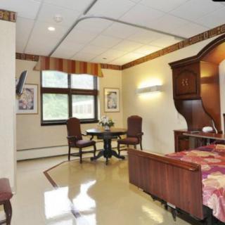 A well-furnished room with a bed, table, and chairs near large windows.