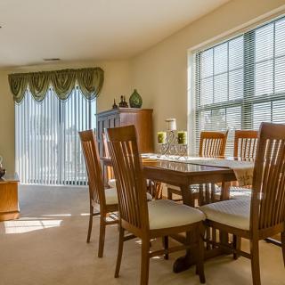 A well-lit dining room with a wooden table and chairs, featuring large windows allowing in natural light.