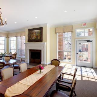 A well-lit dining room with a large table and chairs, featuring a fireplace and chandelier.
