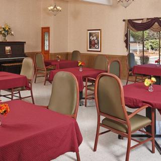 A cozy dining room with red tablecloths and a piano in the corner.