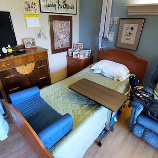 A cozy bedroom featuring a hospital bed, wheelchair, and wooden furniture, adorned with framed artwork on the walls.