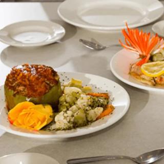 A stuffed green pepper served with a side of vegetables and garnish on a dining table.