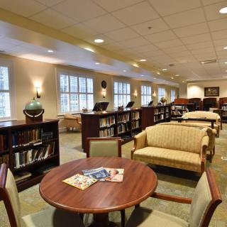 A cozy library interior featuring bookshelves, comfortable seating, and large windows.