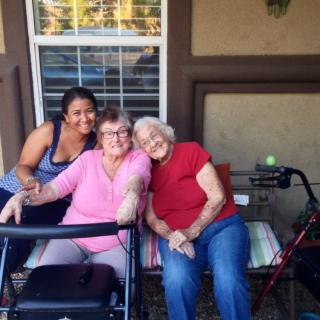 Three women smiling and sitting together on a porch, enjoying a sunny day.