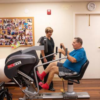 A person exercises on fitness equipment with guidance in a rehabilitation setting.