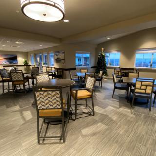 A cozy indoor dining area with tables and chairs, warmly lit with natural light from the windows.