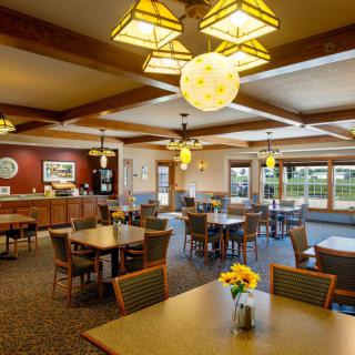 A cozy dining area with wooden tables, comfortable chairs, and warm lighting fixtures.