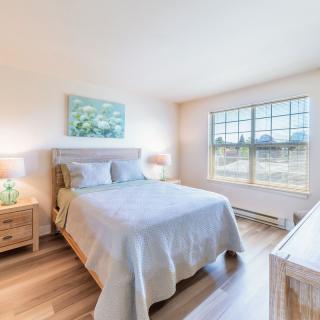 A bright and cozy bedroom featuring a neatly made bed, two bedside tables with lamps, and a large window allowing natural light to fill the room.