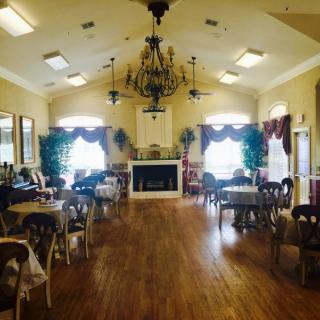 A spacious dining room with a chandelier, neatly arranged tables and chairs, and a fireplace at one end.