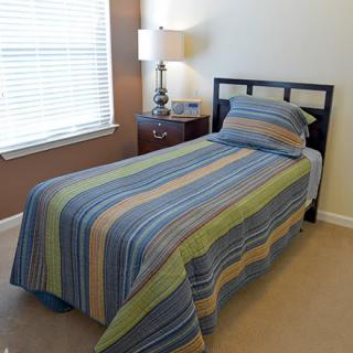 A neatly made single bed with striped bedding next to a lamp and nightstand.