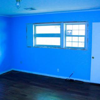 A brightly lit empty room with blue walls and a wooden floor.