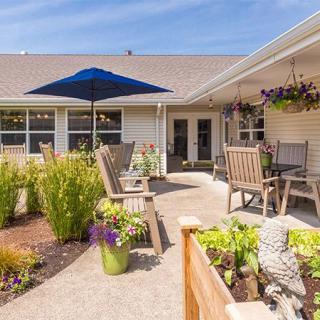 A cozy outdoor patio with comfortable seating, potted plants, and a blue umbrella under a sunny sky.