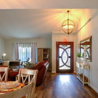 A cozy living room and dining area with a stylish chandelier and wooden flooring, featuring elegant furniture and a decorative front door.