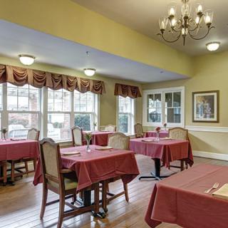 A cozy dining room with tables covered in red tablecloths and a chandelier overhead.