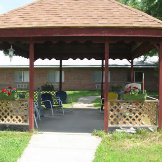 A cozy gazebo surrounded by greenery, featuring seating and vibrant flowers.