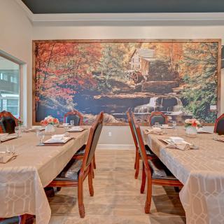 A cozy dining room with two tables covered in tablecloths, set against a large mural depicting a scenic landscape.