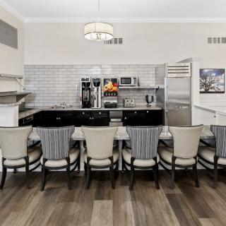 A modern kitchen interior featuring a long dining counter with multiple chairs and sleek appliances.