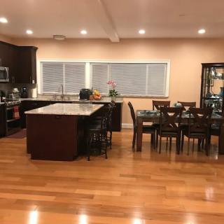 A modern kitchen with an island and adjacent dining area, featuring wooden floors and ample lighting.