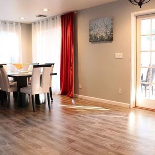 A well-lit dining area with wood flooring, featuring a table and chairs, complemented by curtains and wall art.