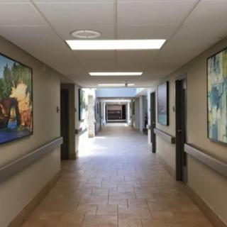 A hospital hallway with art-lined walls and bright lighting leading to another section.