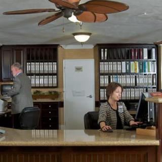 Two people working in an office with bookshelves and a ceiling fan.
