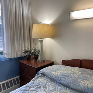 A cozy bedroom setup featuring a bedside lamp, nightstand, and light-colored bedding.