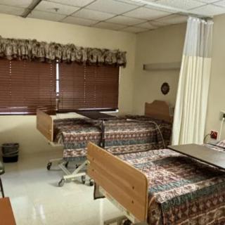 A hospital room with two medical beds, a curtain partition, and window blinds.