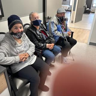 A group of people sitting together in a waiting area, all wearing masks.