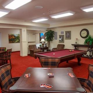 A cozy game room featuring a pool table and card table set against a warmly lit interior.