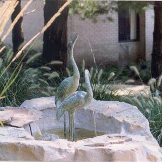 A beautiful sculpture of two birds standing gracefully in a serene garden fountain.