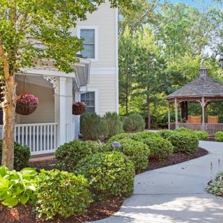 A scenic garden with a winding pathway and a gazebo beside a house.
